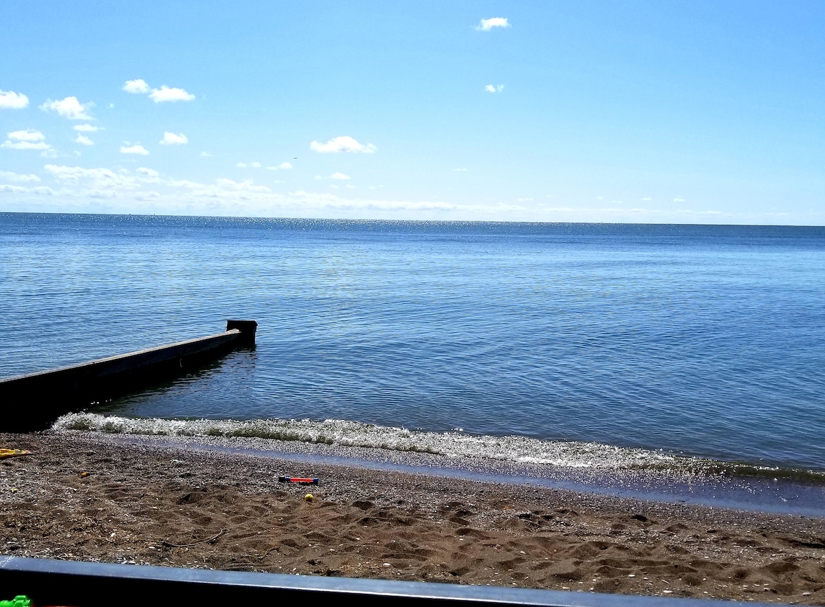 A sandy beach stretches along the calm waters of Lake Erie, reflecting a clear blue sky. Gentle waves lap at the shore, while a wooden pier extends into the lake, inviting leisure activities and relaxation.