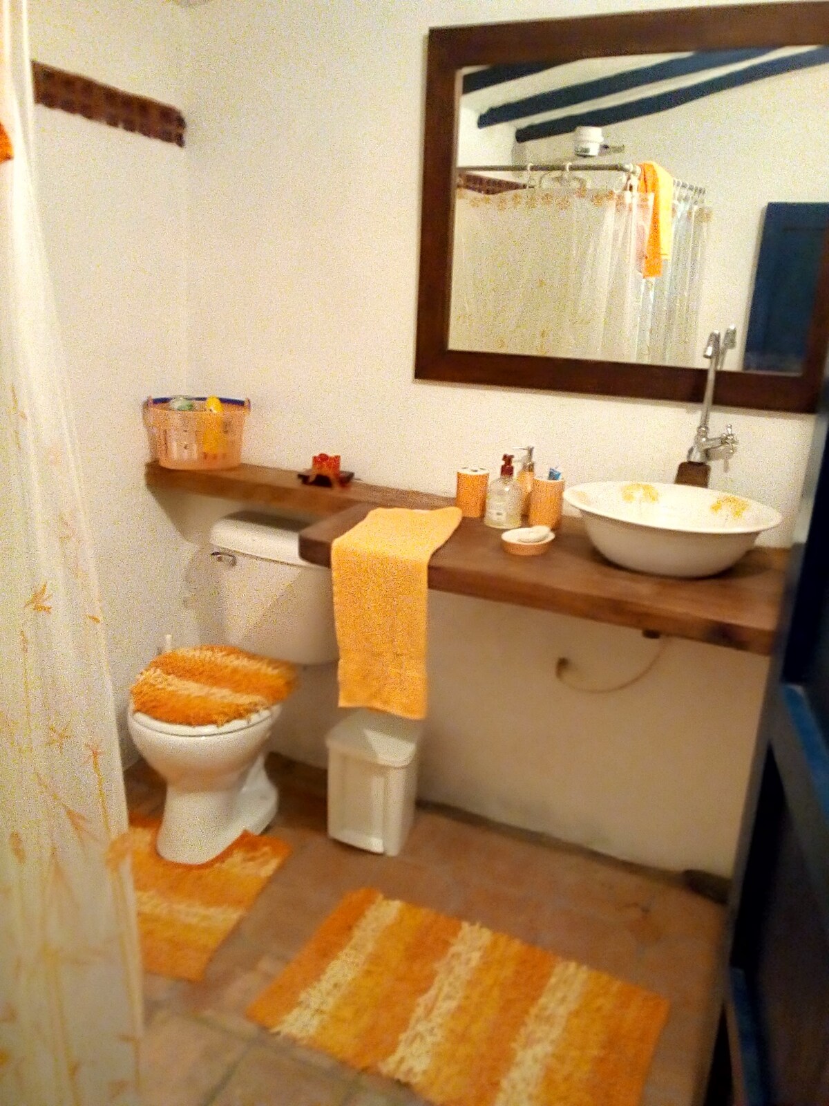 The bathroom features a clean and functional design, highlighted by warm orange towels and decor. A modern sink is positioned atop a wooden counter, while a shower area is enclosed with a curtain. Coordinating mats add comfort to the space, providing an inviting atmosphere.