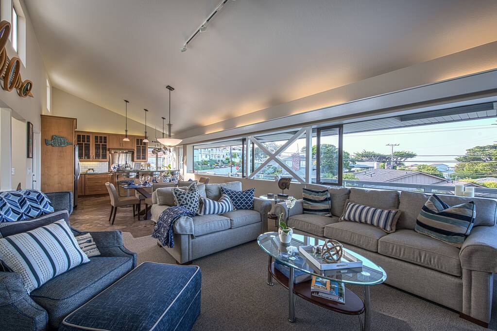 The kitchen, dining area and living room all flow together in an open floor plan, with a gas fireplace at one end of the room and ocean views along the length of the room.