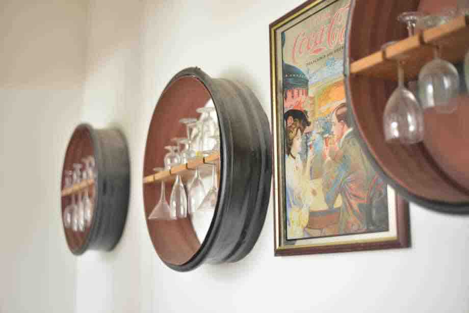 Three circular wall-mounted racks display a selection of glassware, neatly arranged alongside a framed vintage artwork. The design elements contribute to a casual dining atmosphere, with gentle lighting highlighting the unique decor.