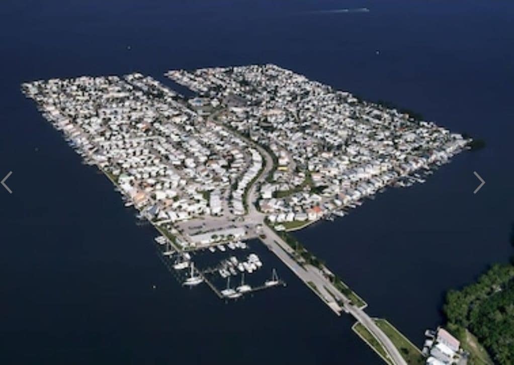 An aerial view of Nettles Island reveals a sprawling community of beach houses set against calm waters. The layout features winding streets and a marina with docks, showcasing the proximity to the water and the organized arrangement of residences.