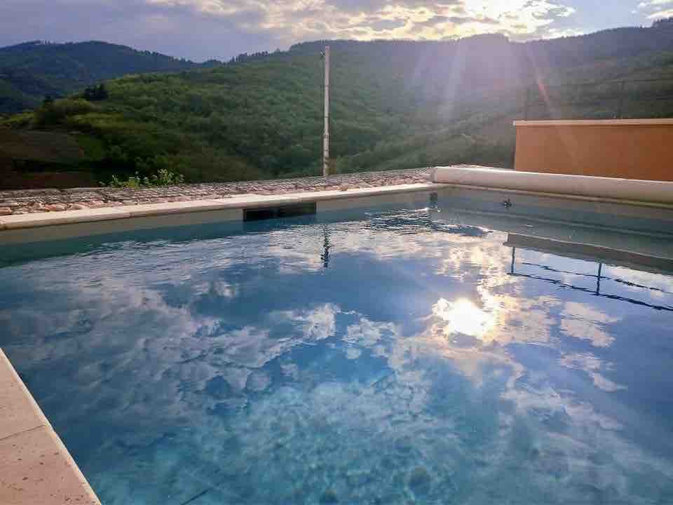 An inviting swimming pool reflects the serene sky and surrounding green hills. Soft light illuminates the water, highlighting its tranquil surface. The pool area is designed for relaxation, seamlessly connecting with the natural landscape.