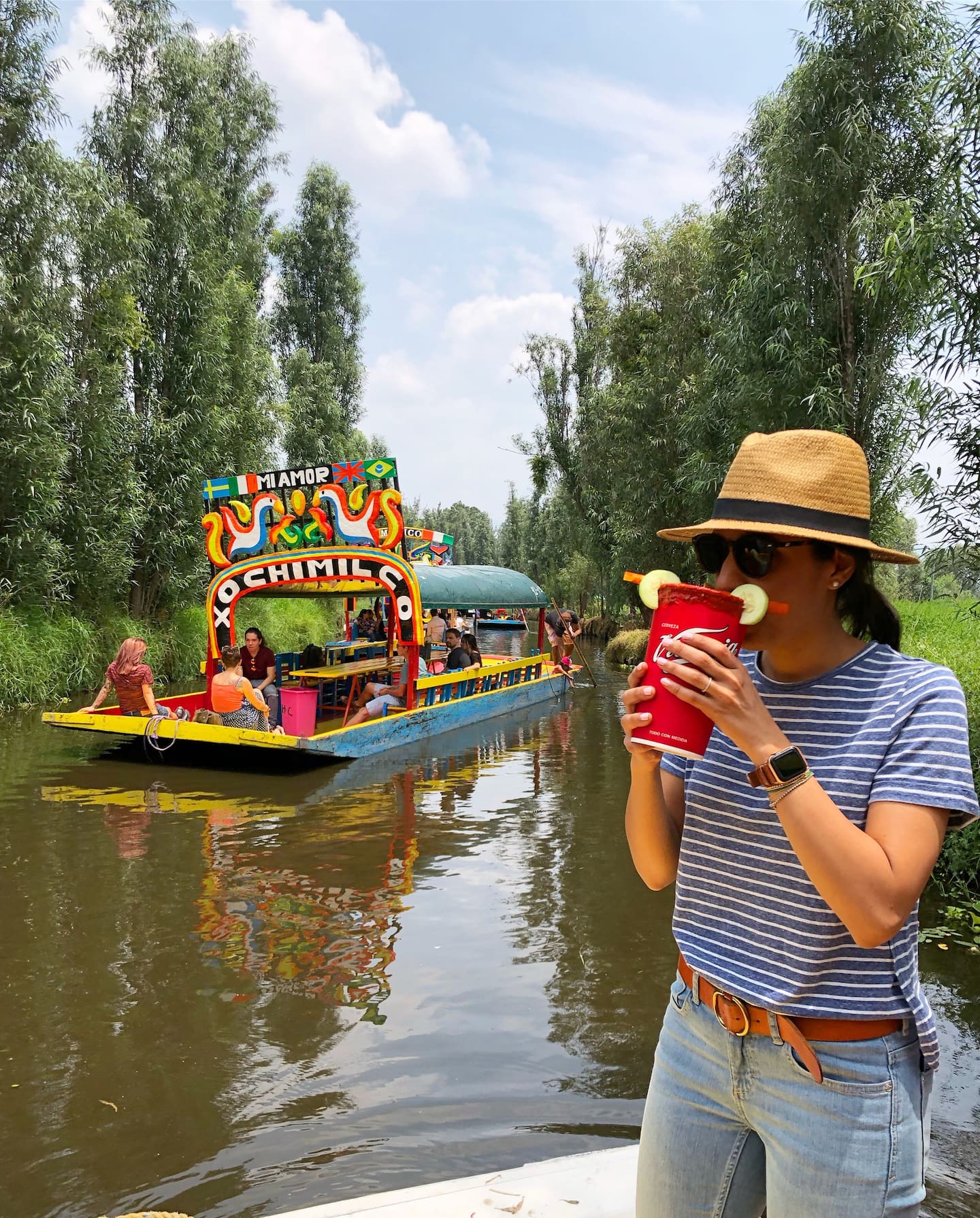 woman drinking out of a cup, sttanding on a trajinera boat in xochimilco, on one of the best xochimilco tours