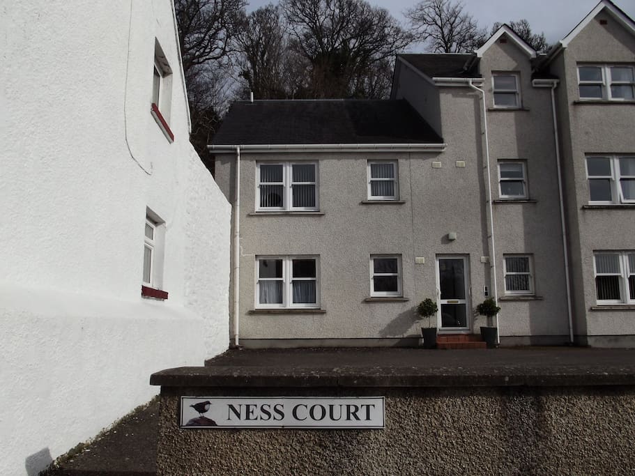 External view of Ness Court showing the entrance door to the apartment with it's free parking space in front. This is a ground floor flat.