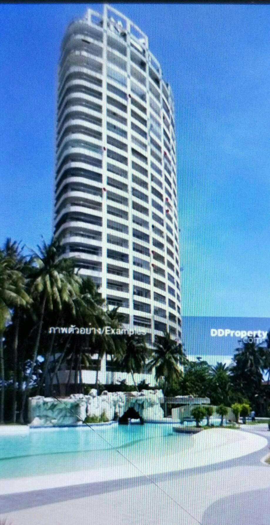 A tall, modern building is showcased against a clear blue sky, surrounded by lush palm trees. The structure features multiple stories and a unique architectural design. A pool area is visible in the foreground, enhancing the appeal of the setting.