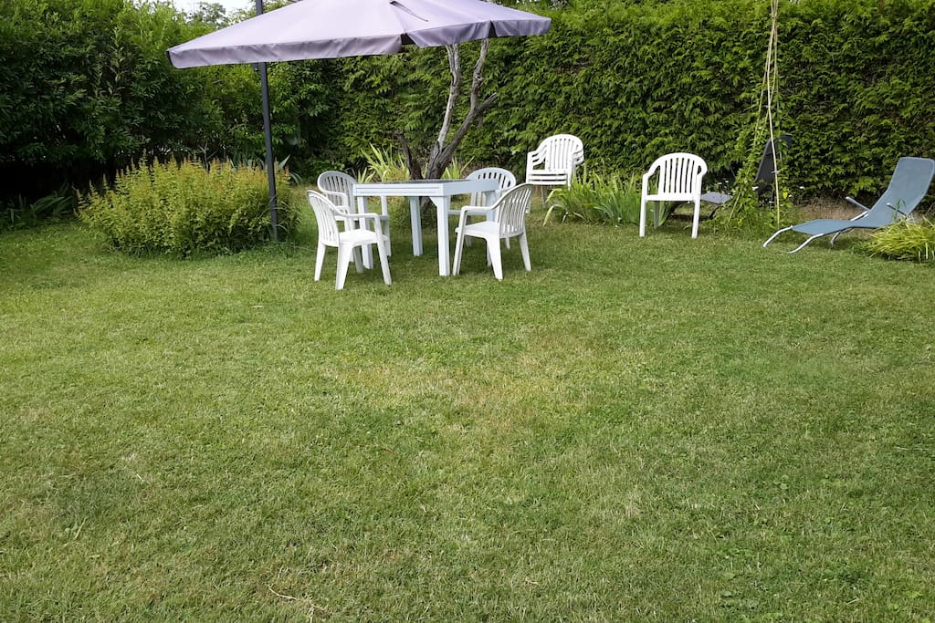 Une pelouse avec table, chaises de jardin, barbecue à disposition