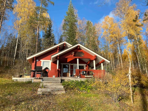A cottage and a wooden sauna by a forest lake.