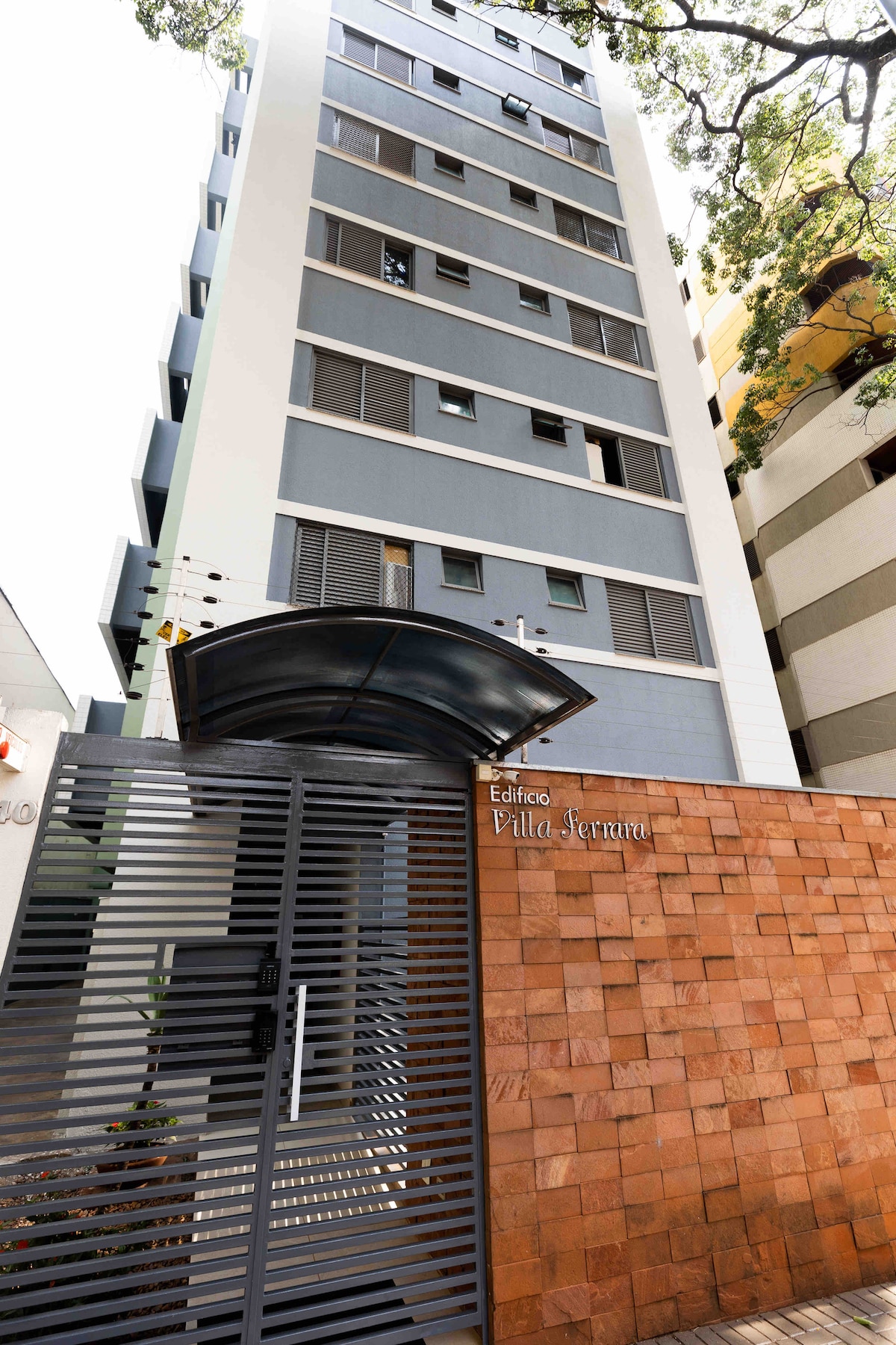 The building facade features a modern design, with a multi-story structure highlighted by large windows. A decorative stone wall is complemented by a sleek metal gate at the entrance, providing a welcoming access point to the residence.