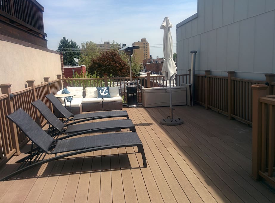 Roof deck with couch, chaise lounges, umbrella and grill.