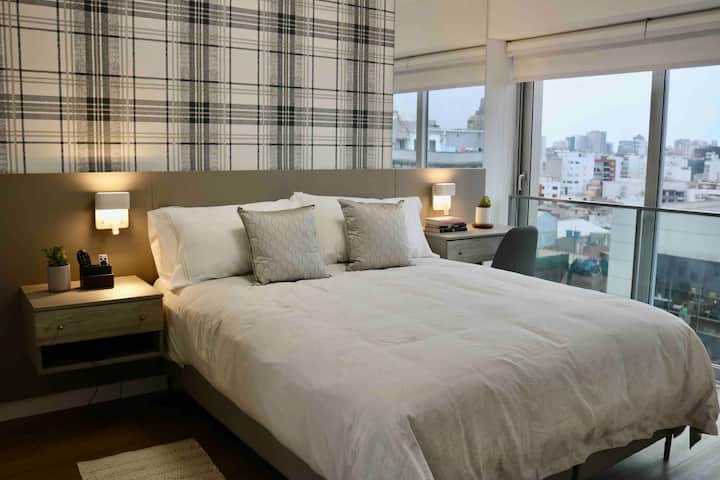 חדר שינה ראשי עם מיטת קווין סייז, שולחן כתיבה, טלוויזיה וארון הליכה עם מגהץ ומגהץ.