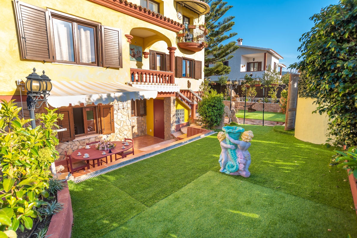 A shared garden area is depicted, featuring a manicured lawn and a charming fountain flanked by two cherubs. A long table with chairs is positioned nearby, and the building's two stories can be seen in the background, showcasing its Mediterranean architecture.