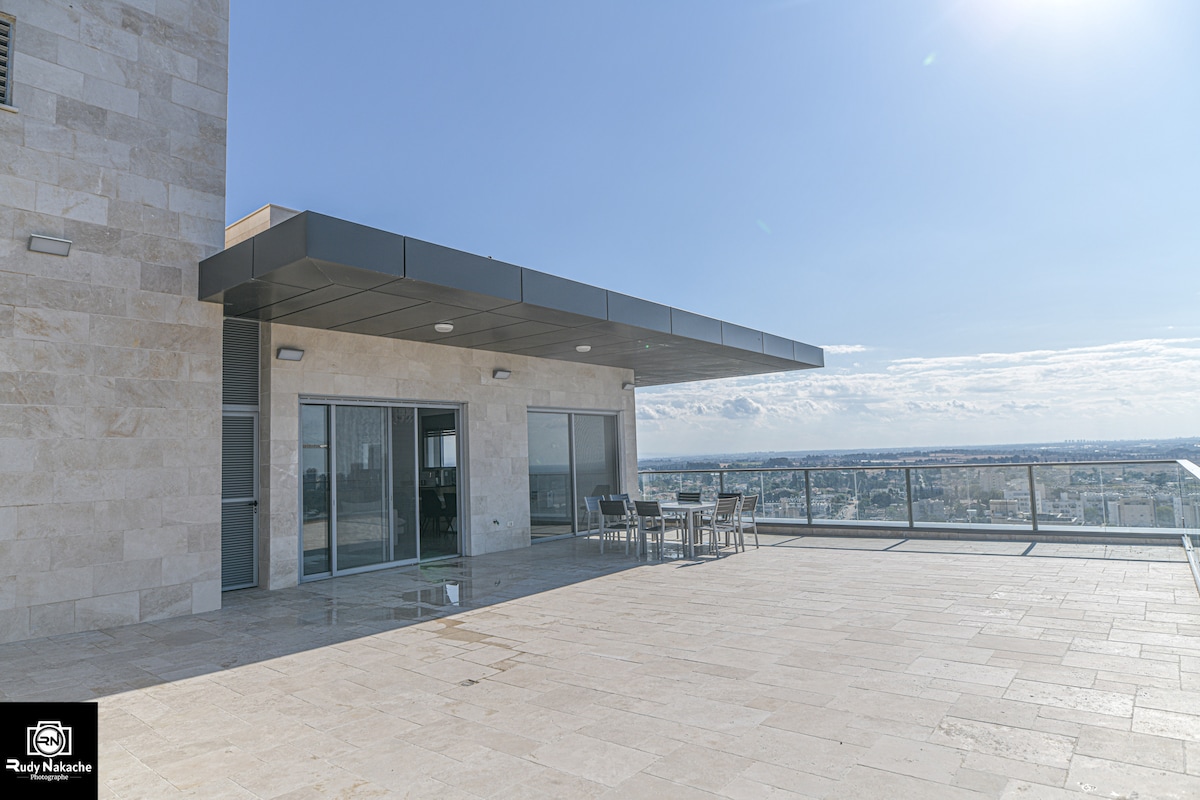 A spacious terrace is highlighted, featuring sleek outdoor furniture. The expansive area is surrounded by a glass railing, providing unobstructed views of the skyline. Light-colored flooring extends across the surface, reflecting the bright atmosphere of the surrounding environment.