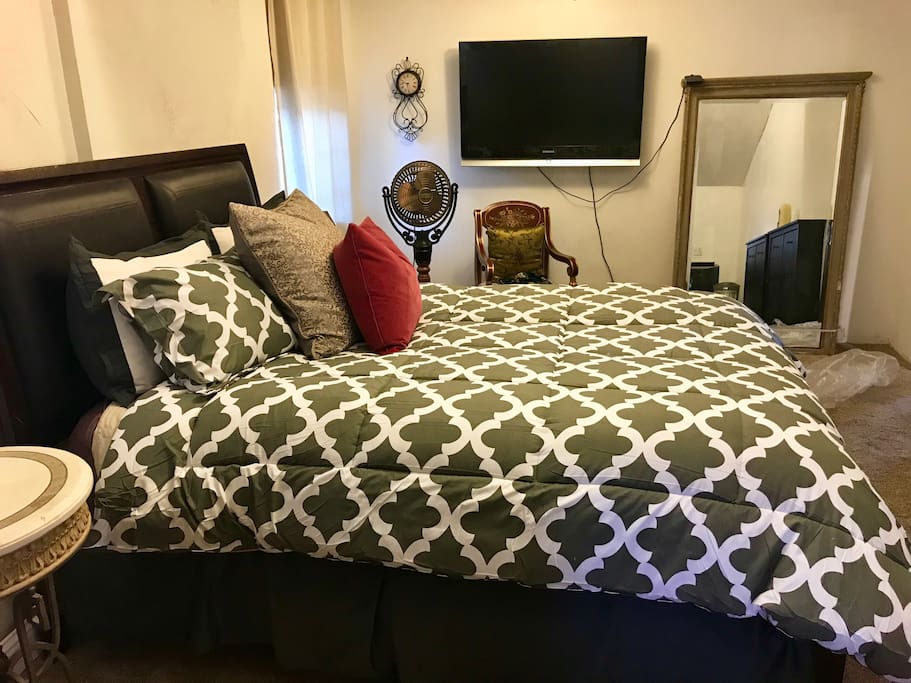 Master bedroom with large screen tv, floor mirror, fan and end table.