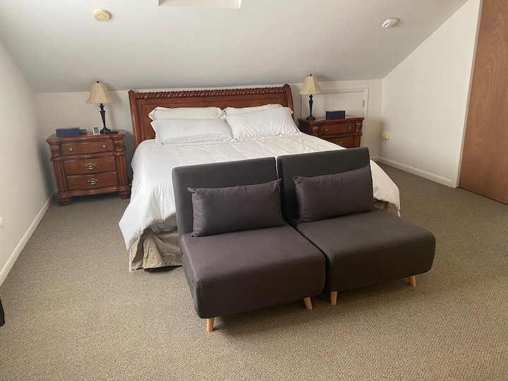 Огромна спална соба на поткровје, со удобни столови за опуштање или за спиење на децата...