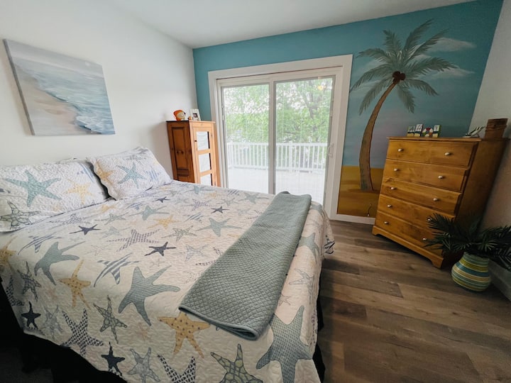 Bedroom with Queen bed, closet, dresser and sliding door to deck. This bedroom also has a mural of a beach. 