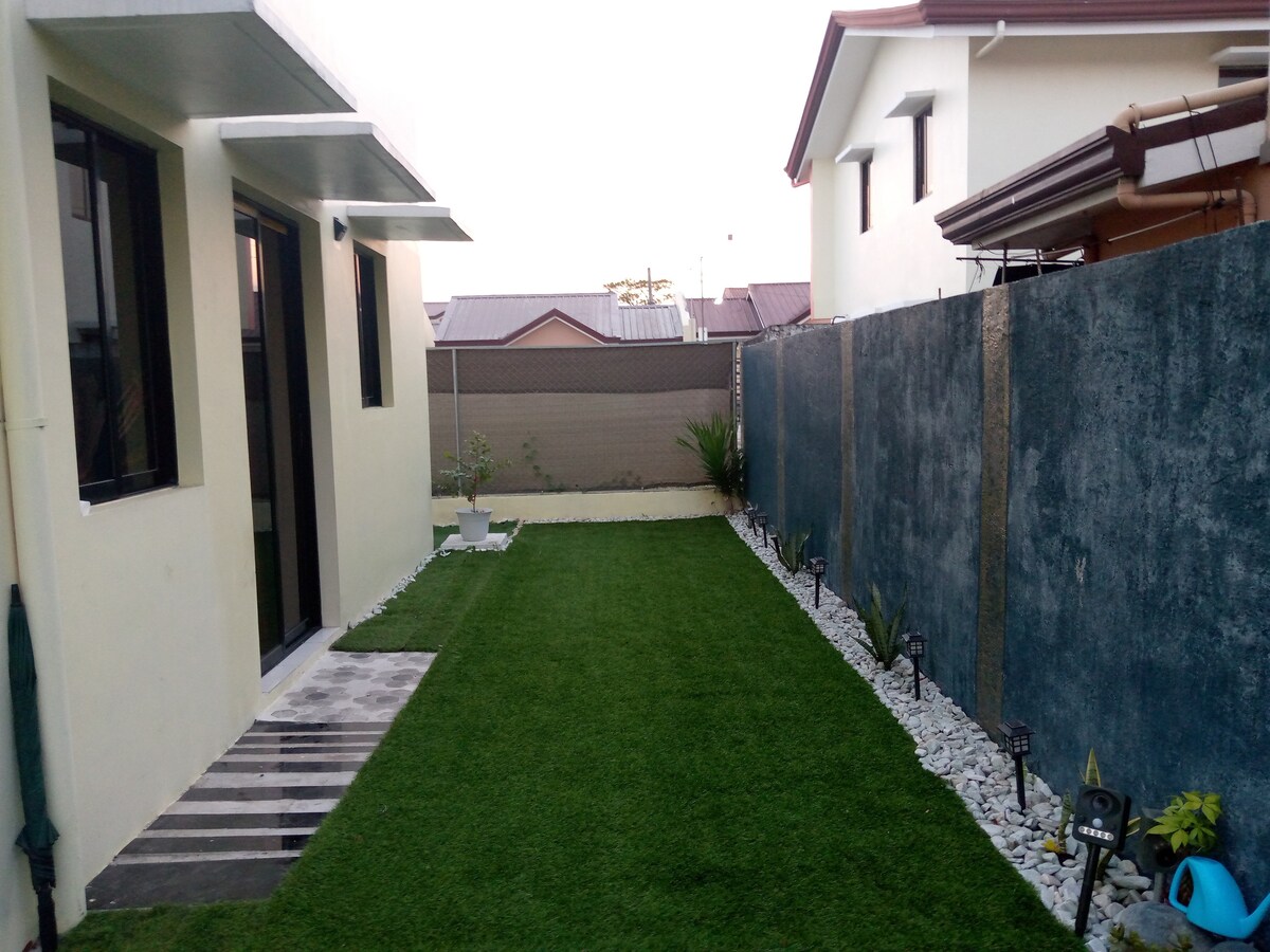 An expansive outdoor area is presented, featuring well-maintained grass and decorative stones lining the pathway. Low landscaping plants are positioned along the edges, with soft lighting enhancing the space. Smooth walls and a clear sky define the serene backdrop of this peaceful retreat.
