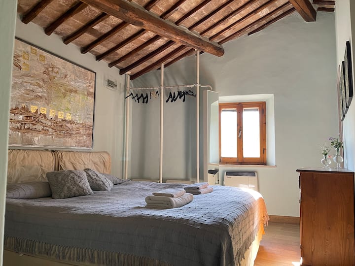 Chambre lumineuse et charmante au premier étage avec salle de bain privée, climatisation et télévision connectée. Les poutres en bois apparentes et la lumière naturelle créent une atmosphère chaleureuse et relaxante, parfaite pour des nuits reposantes dans la campagne toscane.