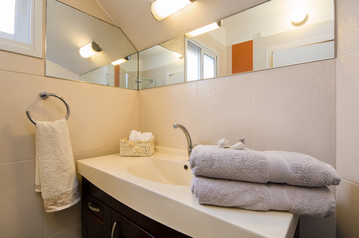 A well-appointed bathroom features a spacious vanity with a sleek countertop, accompanied by neatly stacked plush towels. A stylish mirror reflects natural light from a nearby window, enhancing the clean and modern feel of the space. Ample storage is provided beneath the sink.