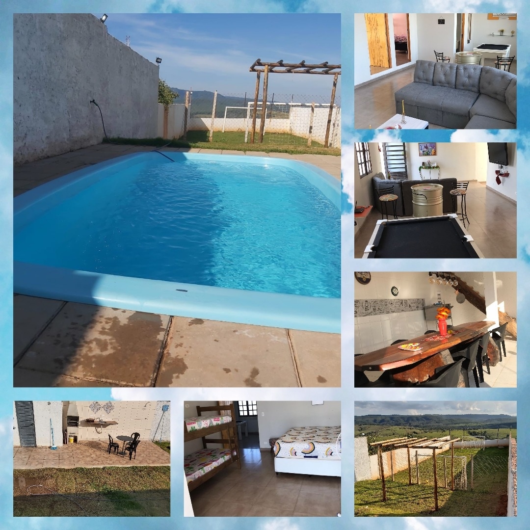 A bright pool glimmers under the sun, surrounded by well-kept grass. A cozy seating area with a sofa is visible, offering comfort. The dining space includes a table and chairs, while a bunk bed is positioned in a nearby room. Scenic countryside views are evident in the background.
