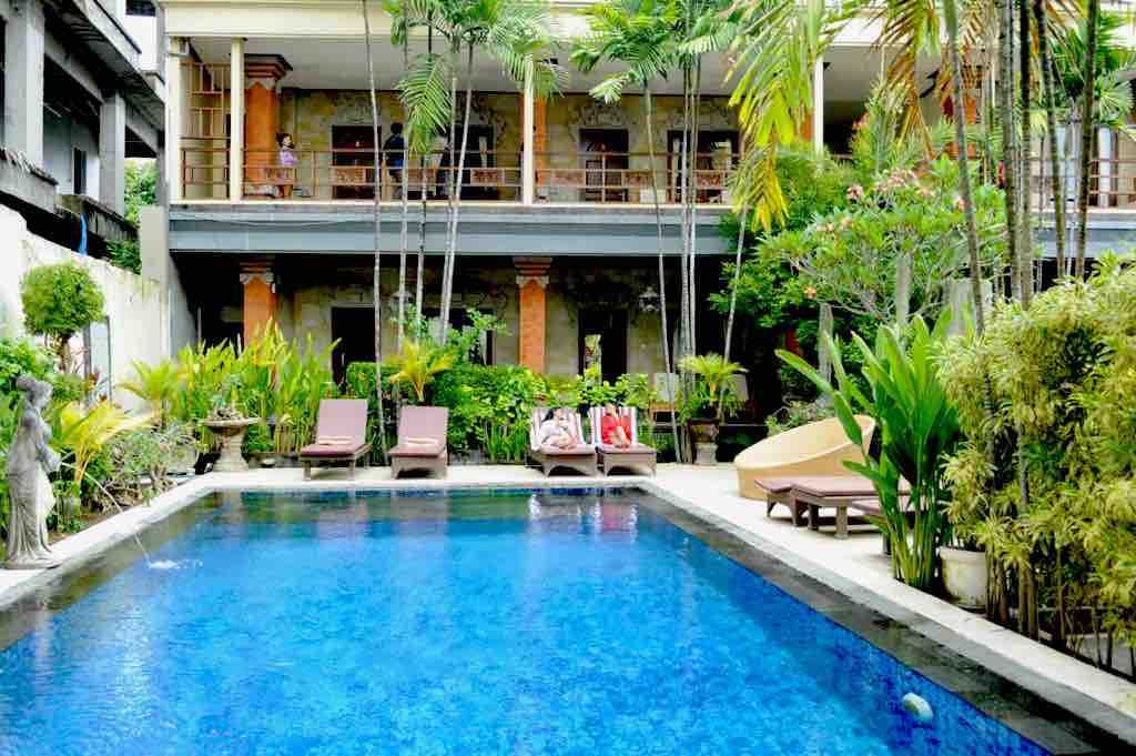 A private swimming pool measuring 14m x 6m is surrounded by lush greenery and deckchairs, creating a relaxing atmosphere. The multilevel building features balconies overlooking the pool area, and a variety of tropical plants is placed strategically around the space.