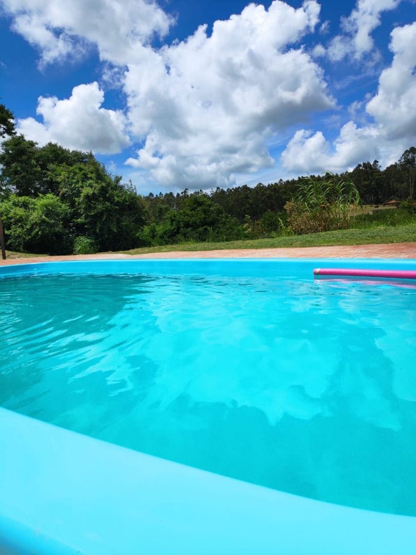 A clear blue pool reflects the sky, surrounded by green foliage and a lawn area. Soft clouds float overhead, creating a calm outdoor setting conducive to relaxation.
