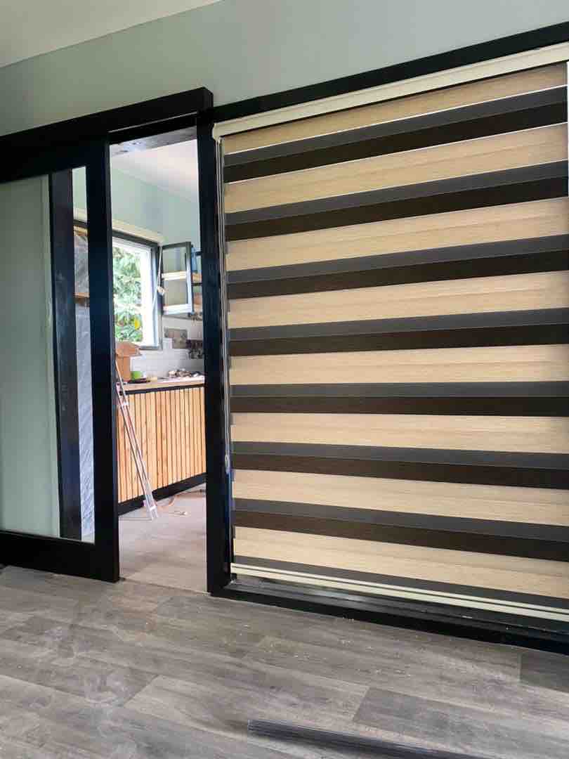 A modern interior view showcases an elegant sliding door adorned with horizontal stripes in a mix of colors. Soft natural light filters in through adjacent windows, illuminating the flooring and hinting at a welcoming kitchen space visible in the background.