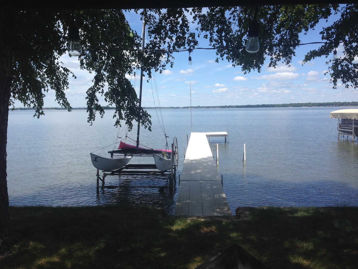 The serene view of Storm Lake features a calm water surface reflecting the sky. A dock extends into the lake, accommodating a small sailboat. Lush green trees create a natural frame, enhancing the peaceful lakeside atmosphere.