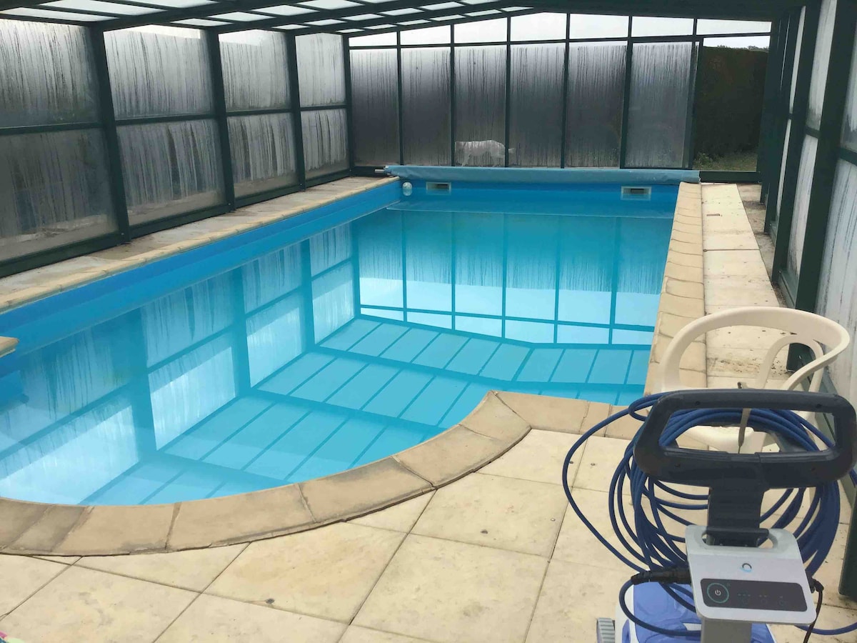 A private indoor pool is featured, surrounded by glass panels that allow natural light to fill the space. The pool's clear blue water reflects the structure above. A pool maintenance device is positioned nearby on the tiled floor, providing convenience for upkeep.