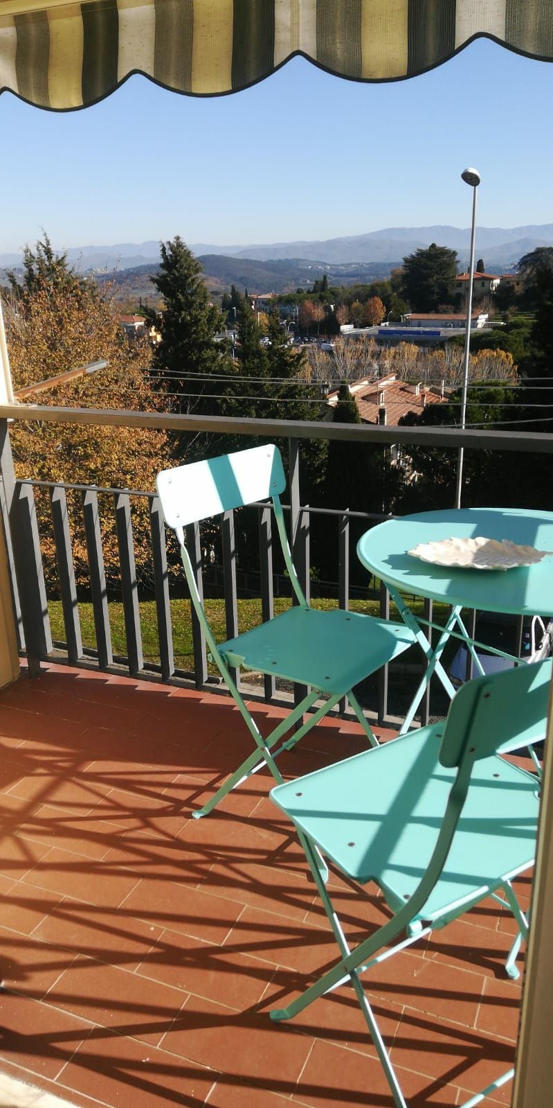 A small balcony showcases a round table accompanied by two light blue chairs. The scenic view of rolling hills and the surrounding landscape is visible, enhancing the outdoor space's relaxation potential.