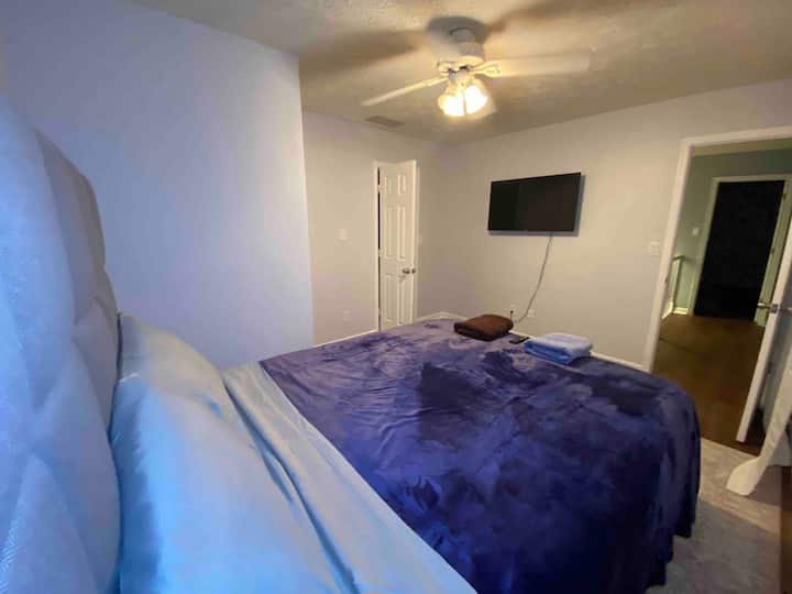 Bedroom 1, queen bed with mounted TV, ceiling fan, and blackout window treatments for restful sleep.