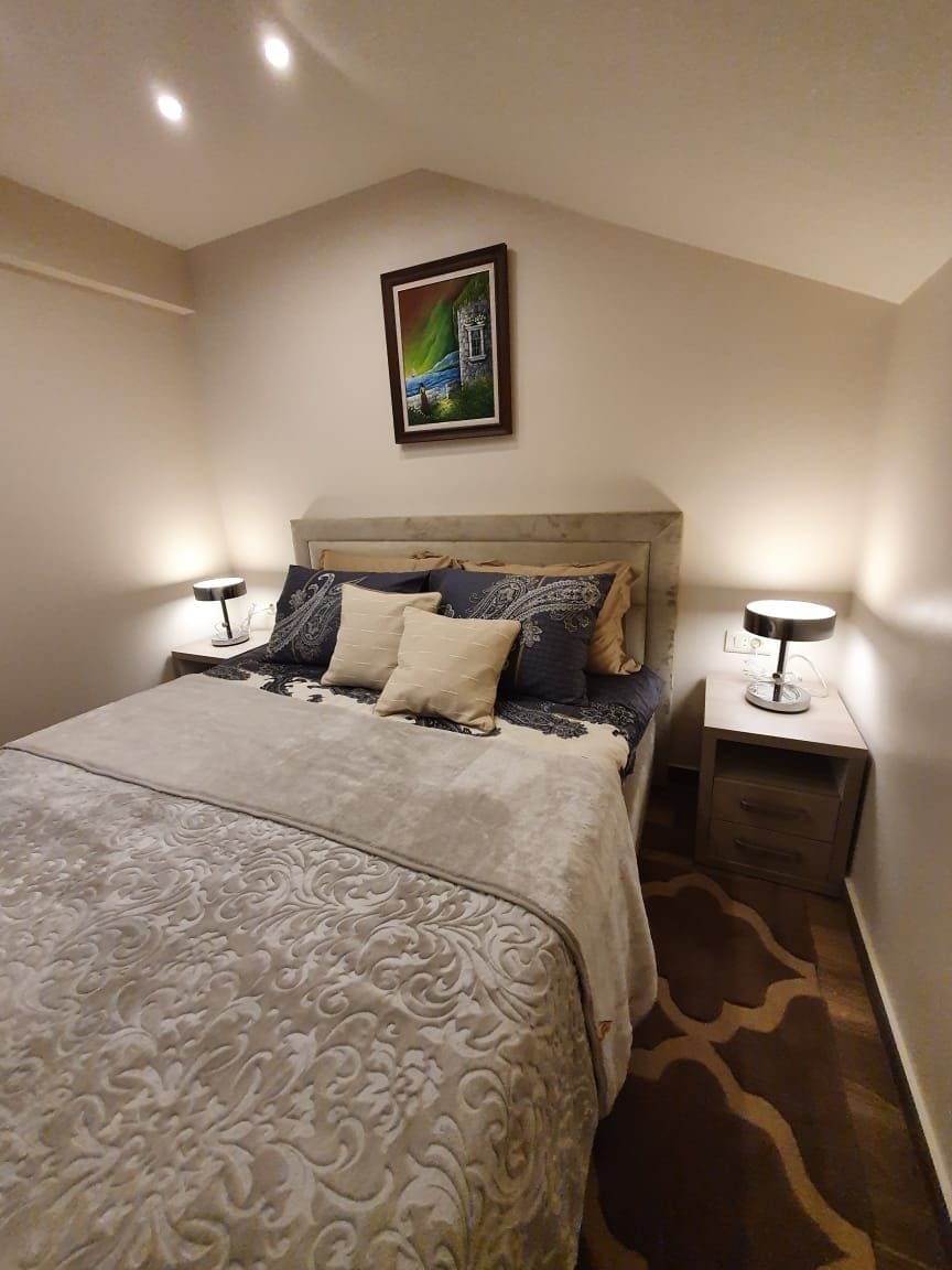 A cozy sleeping area is presented, featuring a spacious bed adorned with decorative pillows and a soft blanket. Two bedside lamps flank the bed, providing soft illumination. A piece of artwork depicting a natural scene is displayed above the headboard, adding visual interest to the room.