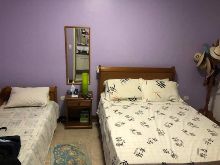 Chumba chenye kitanda cha watu wawili pamoja na kitanda chenye kiyoyozi, televisheni yenye skrini tambarare na kabati la kujipambia