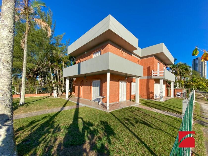 The exterior of a two-story house is showcased, featuring a modern design with alternating layers of light-colored walls and brick. The lush green lawn is bordered by palm trees, and a pathway leads to the entrance, offering a glimpse of the serene surroundings.