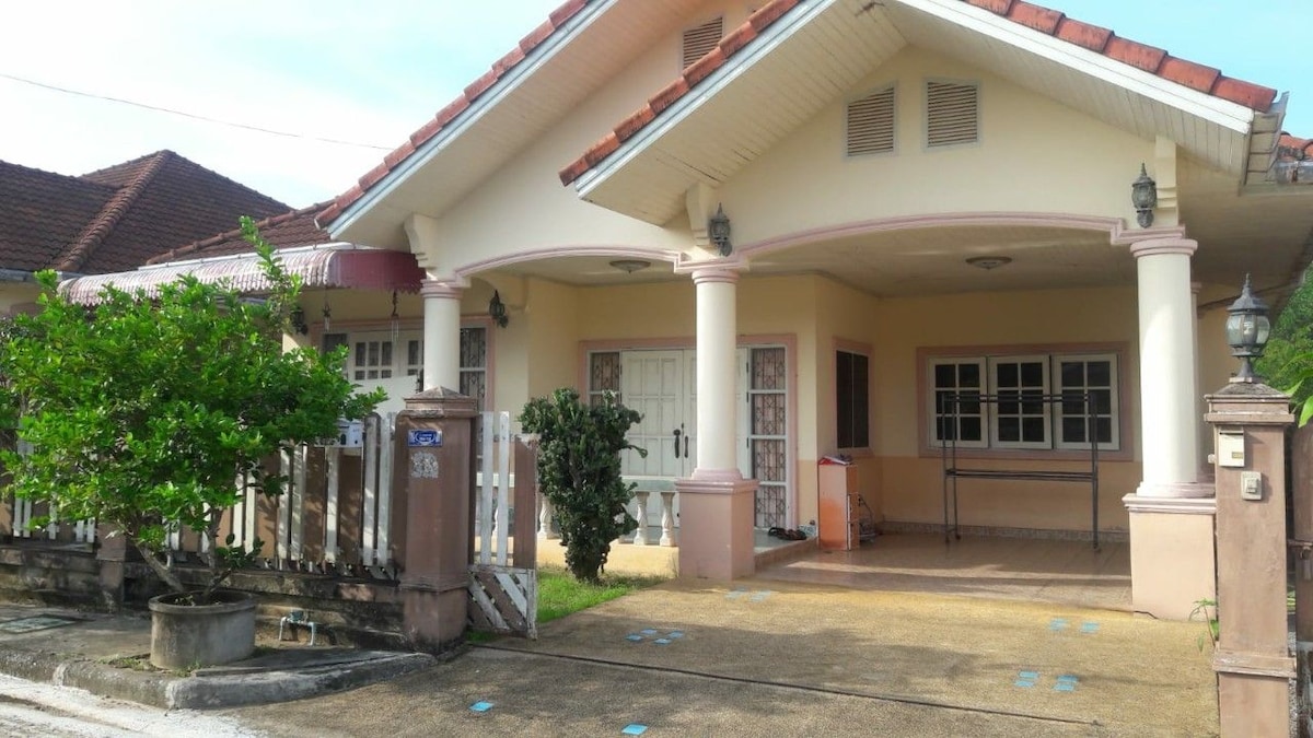 The exterior of the house features a welcoming porch with multiple entry points, flanked by well-maintained greenery. Columns support the roof, while large windows allow natural light to enter. A paved pathway leads to the entrance, enhancing accessibility.