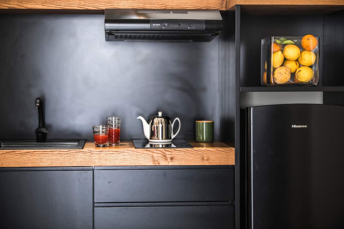 Cucina nera con piano in legno, teiera e un vaso di agrumi