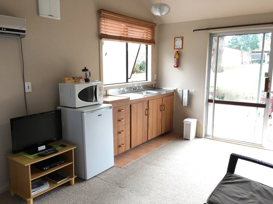 Open plan studio with kitchenette equipped for light cooking, sofa chair and small dining table.