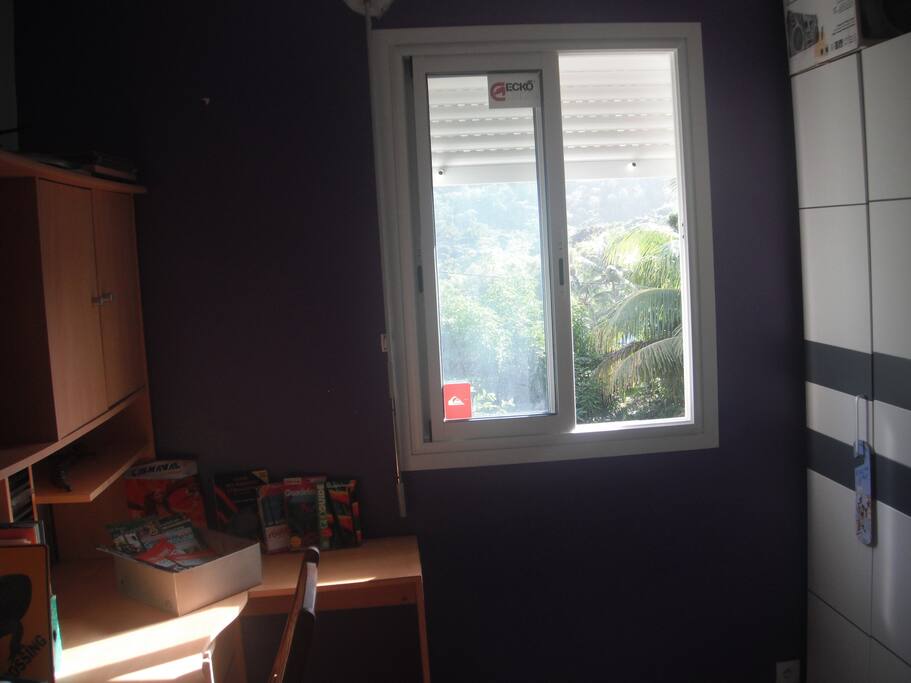 Chambre avec fenêtre sur jardin (fruits offerts selon saison: mangues, fruits de la passion, avocats, goyaves, etc .), bureau et armoire-penderie avec cintres.