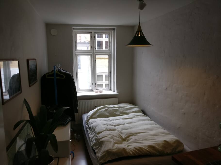 Værelse med seng, kommode og stativ til tøj.