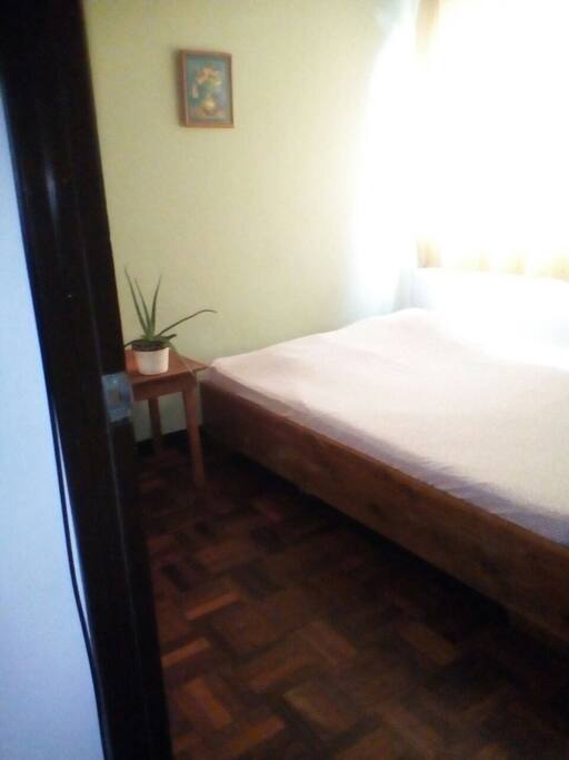 Double-bed next to luminous window and a night table.