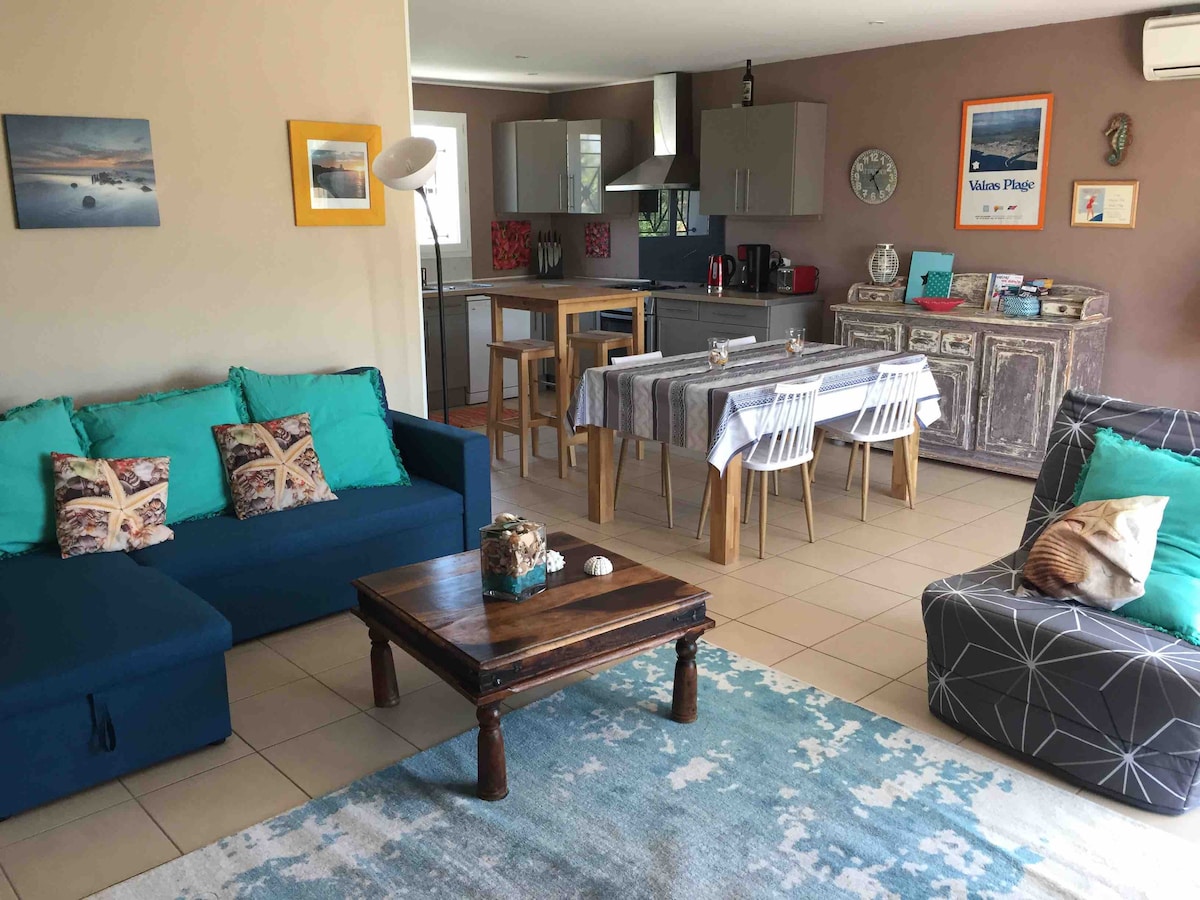 The living area features a cozy seating arrangement with a blue sofa and patterned cushions. A wooden coffee table is positioned centrally on a light blue rug. The dining area includes a table with four chairs, complemented by a modern kitchen in the background.