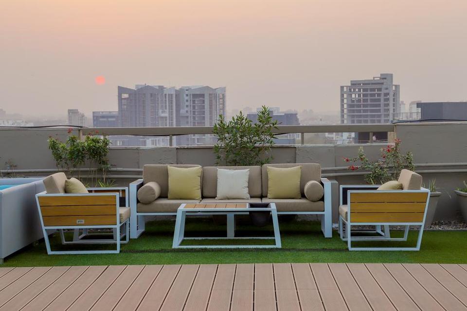 A rooftop terrace is featured, showcasing a comfortable seating area with a sofa and two armchairs arranged around a coffee table. The area is bordered by greenery and a view of the city skyline under an evening sky.