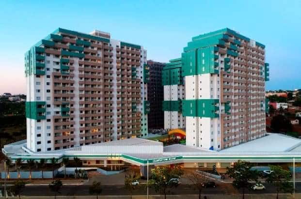 The resort is shown from an elevated perspective, featuring two large towers with a modern design and a color scheme of teal and white. The surrounding area is well-maintained, with palm trees lining the entrance, contributing to a welcoming atmosphere.