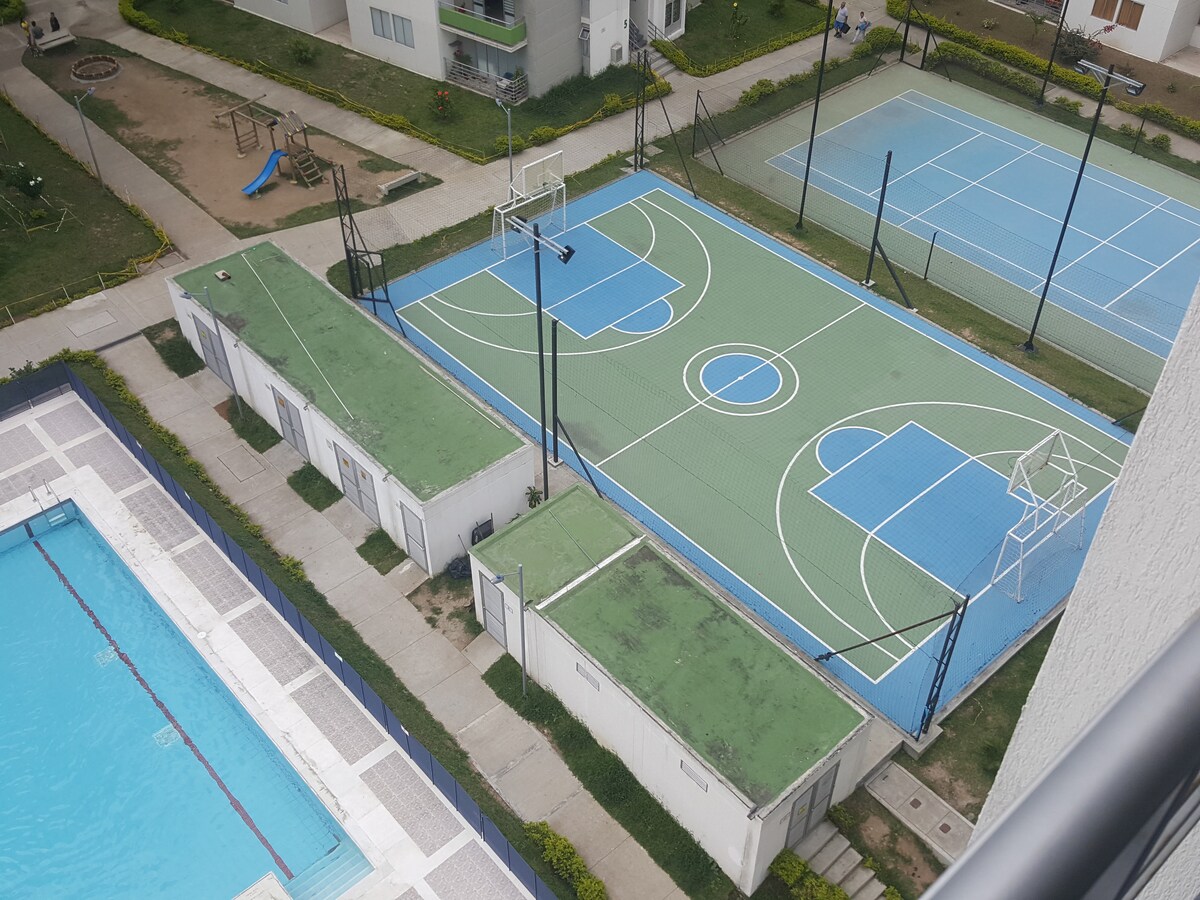 An aerial view captures the expansive recreational facilities of the property, featuring a swimming pool, a multi-sport court with basketball and volleyball areas, and tennis courts. Well-maintained green spaces surround the courts, providing a serene environment for outdoor activities.