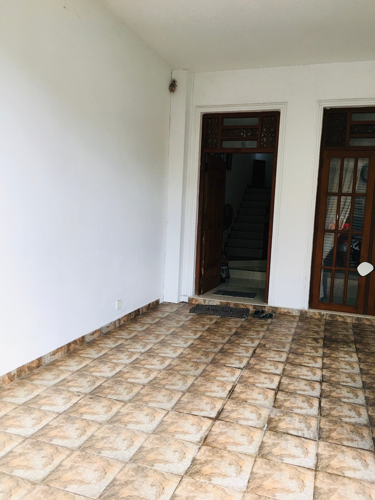 An entrance area features a tiled floor with a neutral pattern, flanked by double wooden doors. A staircase is visible in the background, leading to an upper level. The walls are painted white, providing a clean and open feel.