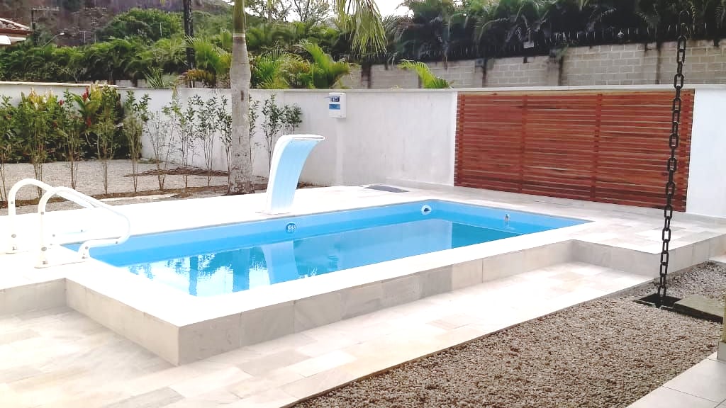 A private swimming pool is surrounded by a neatly landscaped area featuring paving stones and gravel. Lush greenery lines the background, while a wooden privacy screen is visible at the rear. A small water feature adds a touch of elegance to the pool space.