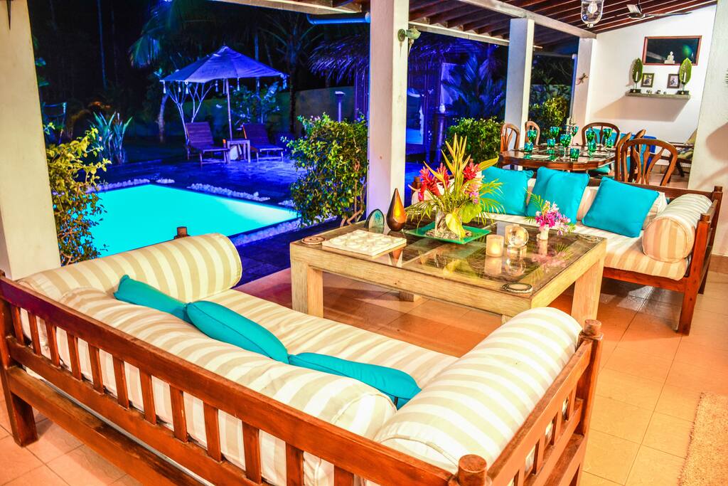 Shaded verandah outdoor living area with sofas, coffee table, dining table & chairs, & ceiling fans. A great outdoor space to relax overlooking the pool and garden