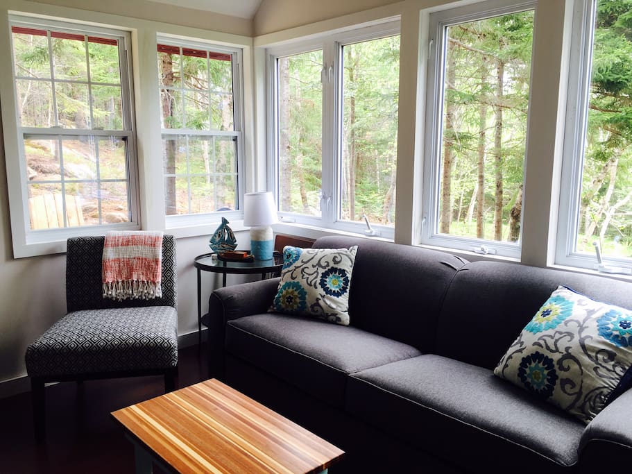 A bright and cozy living room with views of the woods all around you. The couch pulls out to a very comfortable sofa bed.