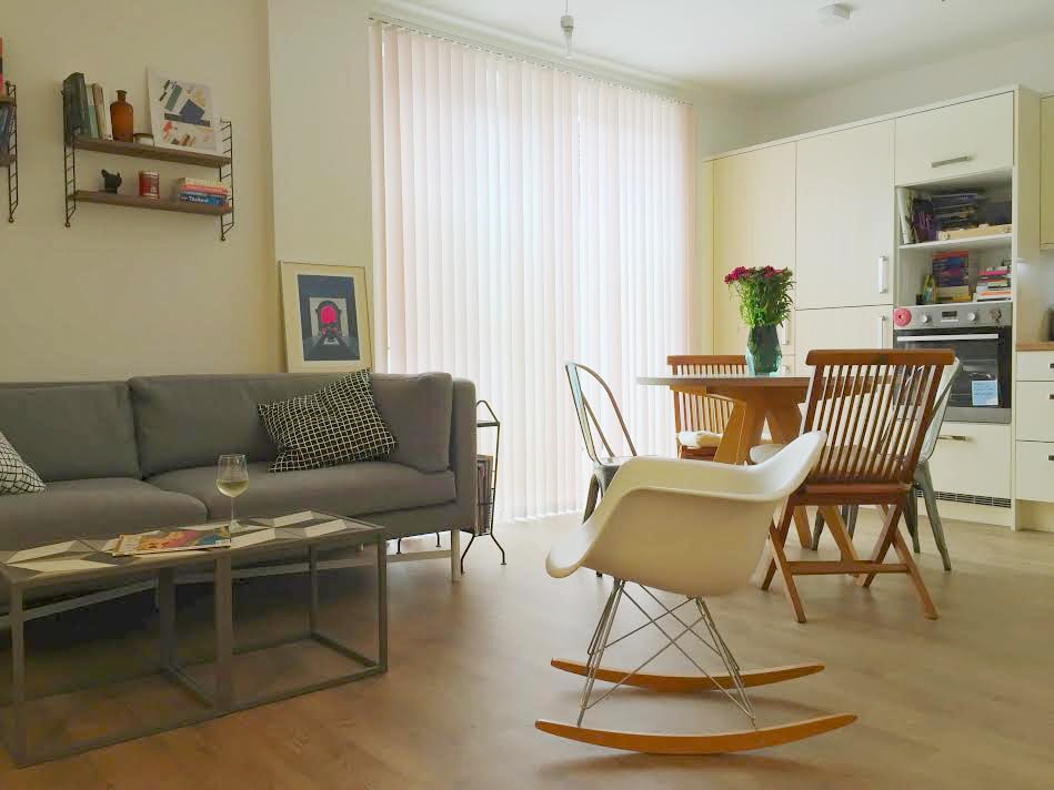 A well-designed living area features a comfortable gray sofa paired with a decorative coffee table. A round wooden dining table is surrounded by four stylish chairs. Floor-to-ceiling light-filtering curtains allow natural light to illuminate the space, enhancing a cozy atmosphere.