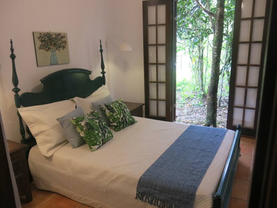 A confortável suíte da casa vermelha abre-se para a área do terreno que preserva a mata atlântica nativa.