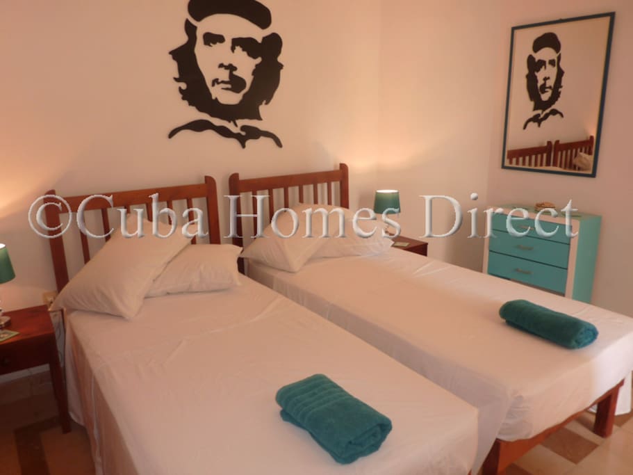 Bedroom with comfy beds, mirror, lamps, set of draws, corner clothes hanger.